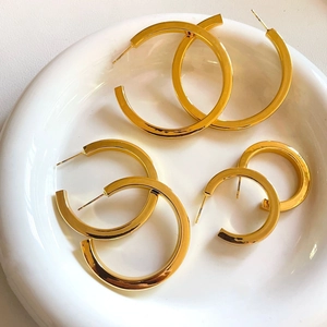 Three pairs of polished gold C-shaped hoop earrings in various sizes on a white ceramic plate