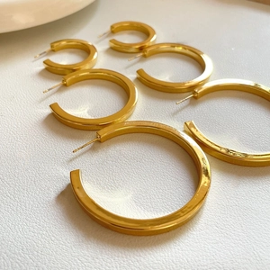 Polished gold C-shape hoop earrings in three sizes on a white textured background