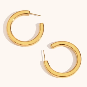 Close-up of thick C-shaped gold hoop earrings with a polished mirror finish on a plain background