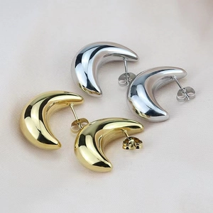 Macro detail of high-polish gold and silver crescent moon earrings on silk fabric