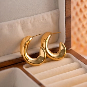 Polished gold hollow C-shaped hoop earrings displayed on a beige velvet jewelry box tray