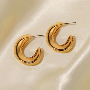 Detailed close-up of chunky gold hollow C-shape earrings on soft cream velvet fabric