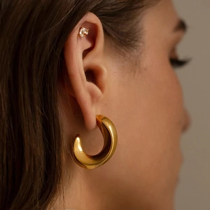 Polished gold hollow C-shaped earrings paired with crystal stud on model's ear