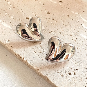 Polished silver heart stud earrings in 18K gold plated copper on a stone background