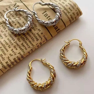 Detailed close-up of twisted hoop earrings with zircon inlays in silver and gold