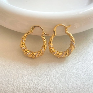 Detailed close-up of golden twisted hoop earrings with sparkling micro-paved cubic zirconia