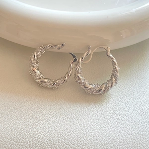 Close-up of silver twist hoop earrings with pavé zircons on a white leather surface