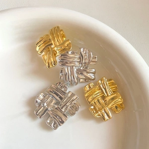 Close-up of woven knot metal earrings in gold and silver finish on a ceramic plate