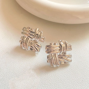 Macro shot of silver woven knot earrings on white leather background showing fine texture