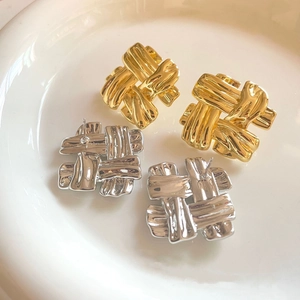Detailed view of gold and silver woven square earrings displayed on a white ceramic plate
