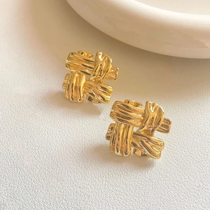 Detail shot of golden square braided earrings with polished finish on white leather background
