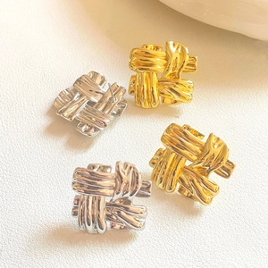 Chic woven knot stud earrings in gold and silver finish on white leather background