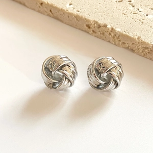 Polierte silberne Knoten-Ohrstecker auf minimalistischem beigem Stein-Hintergrund