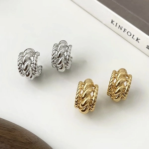 Détail macro de boucles d'oreilles torsadées en C or et argent sur table blanche