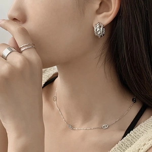 Détail de boucles d'oreilles créoles argentées et collier épais sur un mannequin