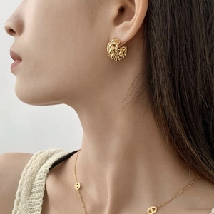 Gros plan de créoles dorées torsadées et d'un collier fin portés par un mannequin