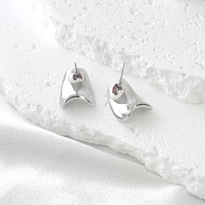 Minimalist irregular wavy silver stud earrings on white stone and silk background