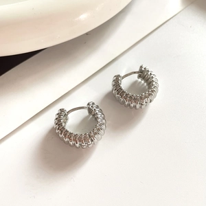 Close-up of silver-tone ribbed spiral hoop earrings with polished metallic texture