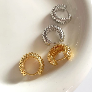 Polished gold and silver croissant hoop earrings with ribbed texture on ceramic plate
