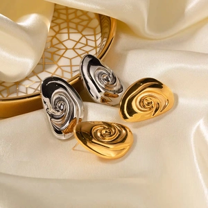 Macro shot of 18K gold and silver spiral water drop earrings on soft cream silk fabric