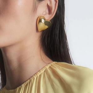 Polished 18K gold plated heart stud earrings shown on model with shiny metallic finish