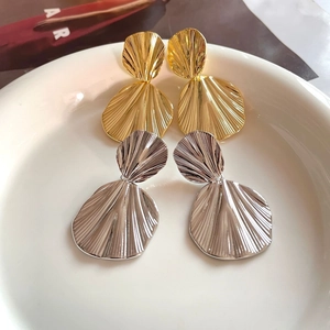 Macro detail of fan-shaped pleated metal earrings in polished gold and silver finish