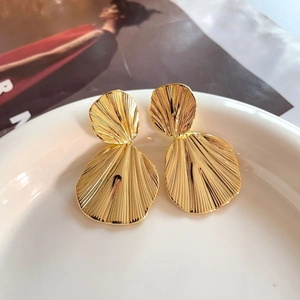Detailed close-up of gold-plated double fan earrings with pleated texture on white ceramic
