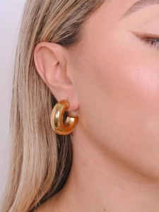 Detail of chunky gold-plated C-shape hoop earring worn on model for a trendy look