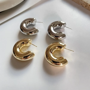 Detailed view of glossy gold and silver chunky C-shaped hoop earrings on a tray