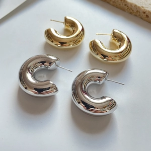 Macro shot of chunky C-shaped hoop earrings in polished gold and silver metallic finishes