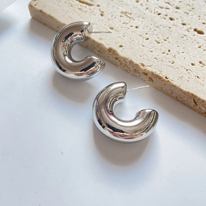 Detailed macro view of silver-plated C-shaped chunky hoop earrings on stone background