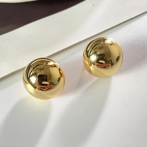 Détail de boucles d'oreilles boules dorées avec finition polie miroir sur fond blanc pur