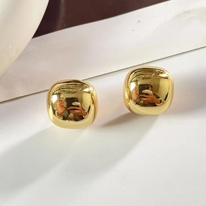 Gros plan de boucles d'oreilles carrées dorées polies aux bords arrondis sur socle blanc