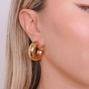 Polished 18K gold plated thick C-shaped hoop earrings worn by a model in a close-up view