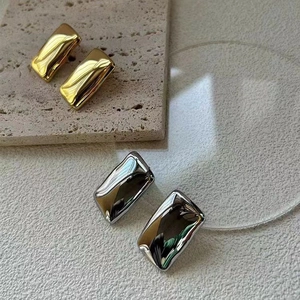 Detail of geometric rectangular earrings in gold and silver with wavy metal texture