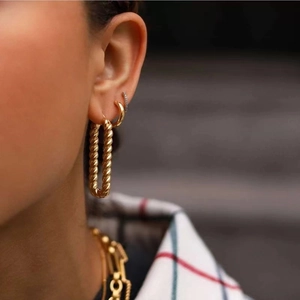 Fashionable gold twisted hoop earrings with chunky geometric weave design on a model