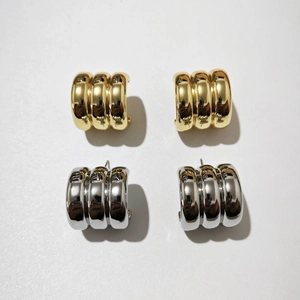 Close-up of chunky gold and silver ribbed C-shaped hoop earrings in high-polish finish