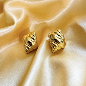 Detailed macro view of 18K gold-plated conch earrings on elegant champagne silk fabric