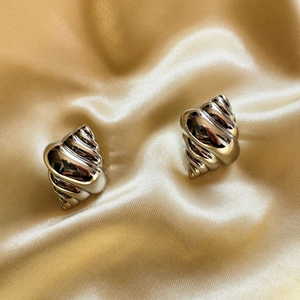 Polished silver conch shell stud earrings on luxurious golden silk fabric background