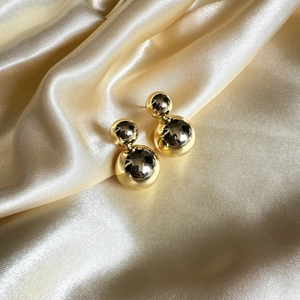 Boucles d'oreilles boules doubles dorées brillantes sur fond élégant en soie de champagne