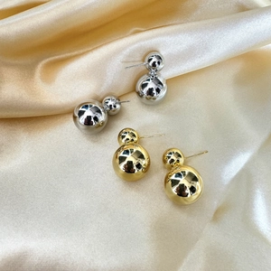 Détail de boucles d'oreilles double boule argentées et dorées sur satin de luxe