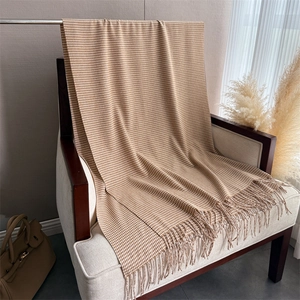 Dettaglio di sciarpa con motivo pied de poule beige e marrone e frange su sedia