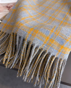 Detailed close-up of soft plaid scarf fabric with orange accents and fringe edges