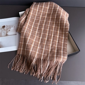 Detailed close-up of brown plaid scarf with fringe tassels on a black gift box