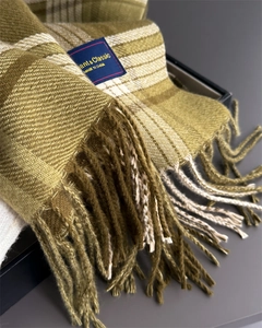 Close-up of olive green and beige plaid scarf with tassels and an elegant fabric label