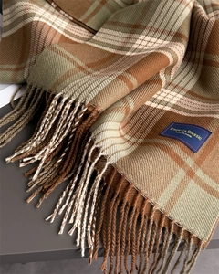 Close-up of fringe tassels and woven label on a plaid cashmere-like warm winter scarf