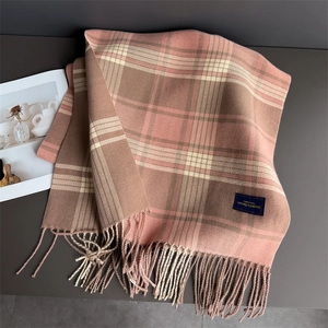 Detail of plaid scarf with soft fringe and elegant classic woven label on tabletop
