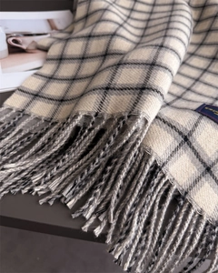 Close-up of beige plaid scarf with soft fringe edges and woven brand label detail