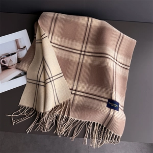 Close-up of classic brown plaid scarf with fringe and elegant gold-lettered woven label
