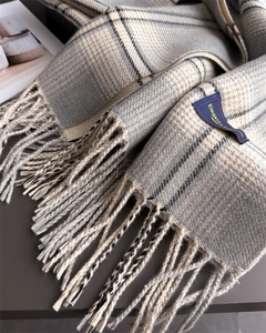 Close-up of gray and white plaid scarf featuring soft fringe and elegant woven label